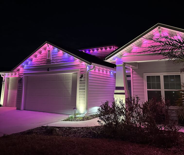 Two-story home and palms washed in purple with a lit brick driveway