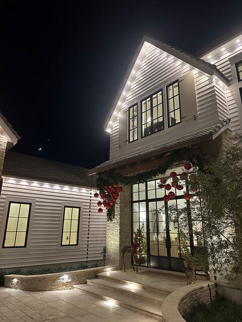 White two-story home with warm white roofline lights and lit front steps