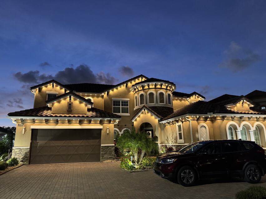 Stucco home at dusk with warm white lights along every roofline