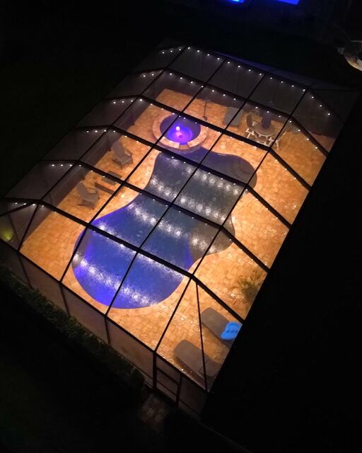 Aerial view of a pool enclosure lit warm white with blue pool lighting